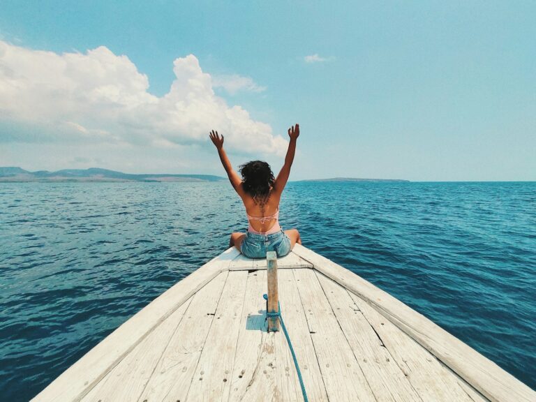 Home 4 woman wearing blue denim short-shorts sitting on boat raising hands